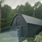 Gray barn in a wooded area.