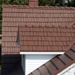 Brown shingle roof with chimney and white siding.