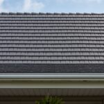 Close-up of shingled house roof under blue sky.