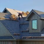 Worker installing roofing shingles on house.